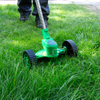 Személy zöld fűszegélynyírót használ kerekekkel a fű vágás ához.